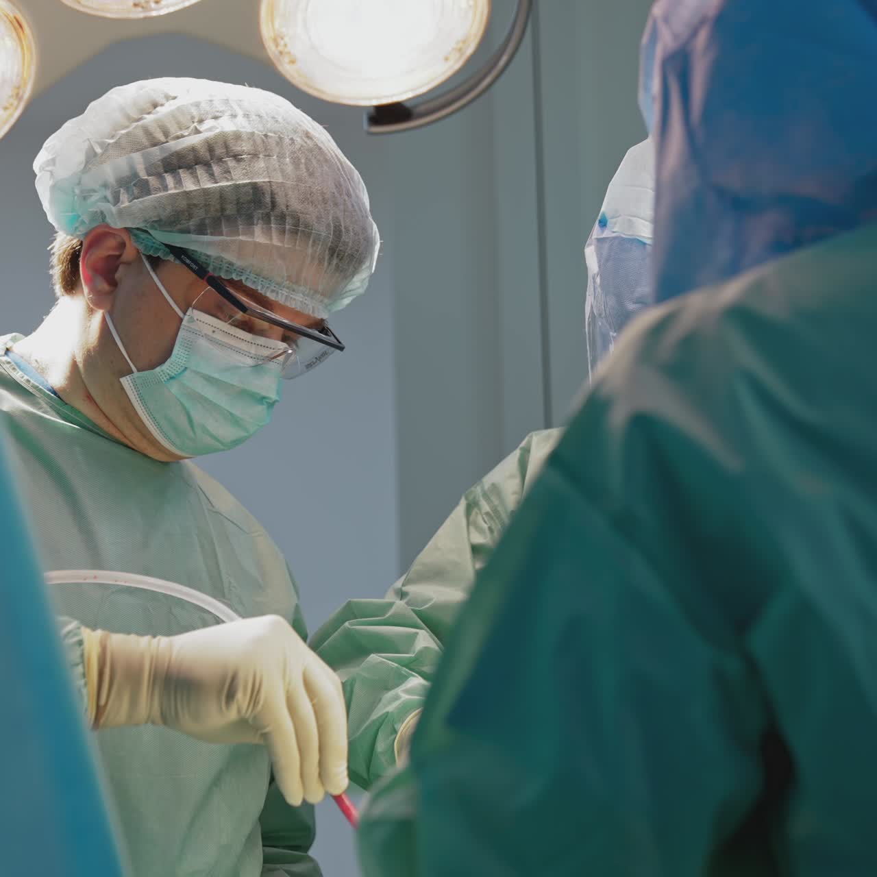 Team of medical workers perform a surgery. Surgeons in protective uniform and mask work with medical instruments in clinic saving patient's life. Health care concept