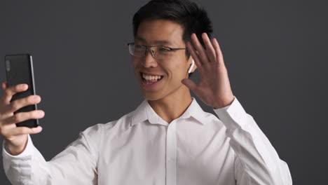 asian man in earphones having a video call on smartphone.