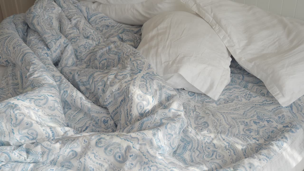 cama sin hacer con ropa de cama azul y blanca