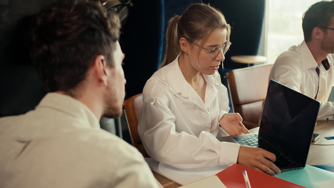 una chica rubia con gafas en una camisa blanca muestra su proyecto en una computadora portátil a un gerente en una camisa blanca