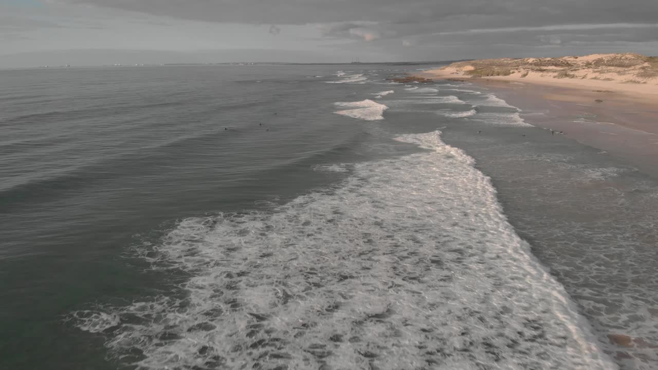 Surfers trying to catch waves, scenic Atlantic coastline of Portugal; drone