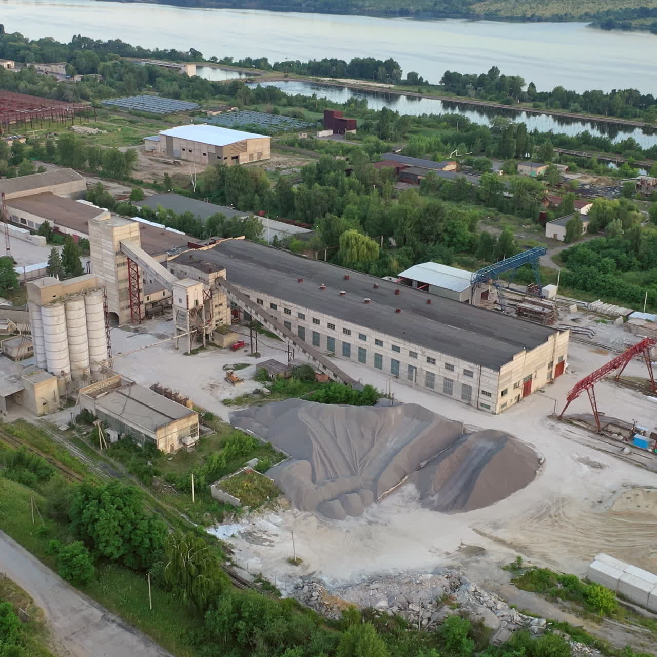 Construction site from bird's eye near the river. Buildings of industrial factory on the bank of the river. Aerial view.