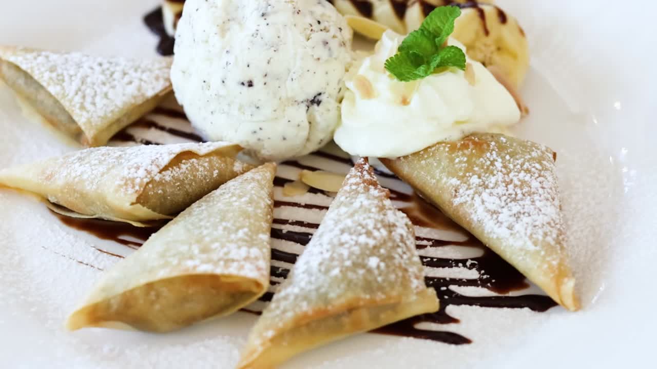 A beautifully plated dessert featuring samosas, mint garnish, and ice cream with chocolate drizzle.