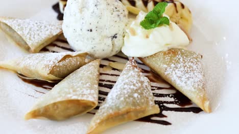 a beautifully plated dessert featuring samosas, mint garnish, and ice cream with chocolate drizzle.