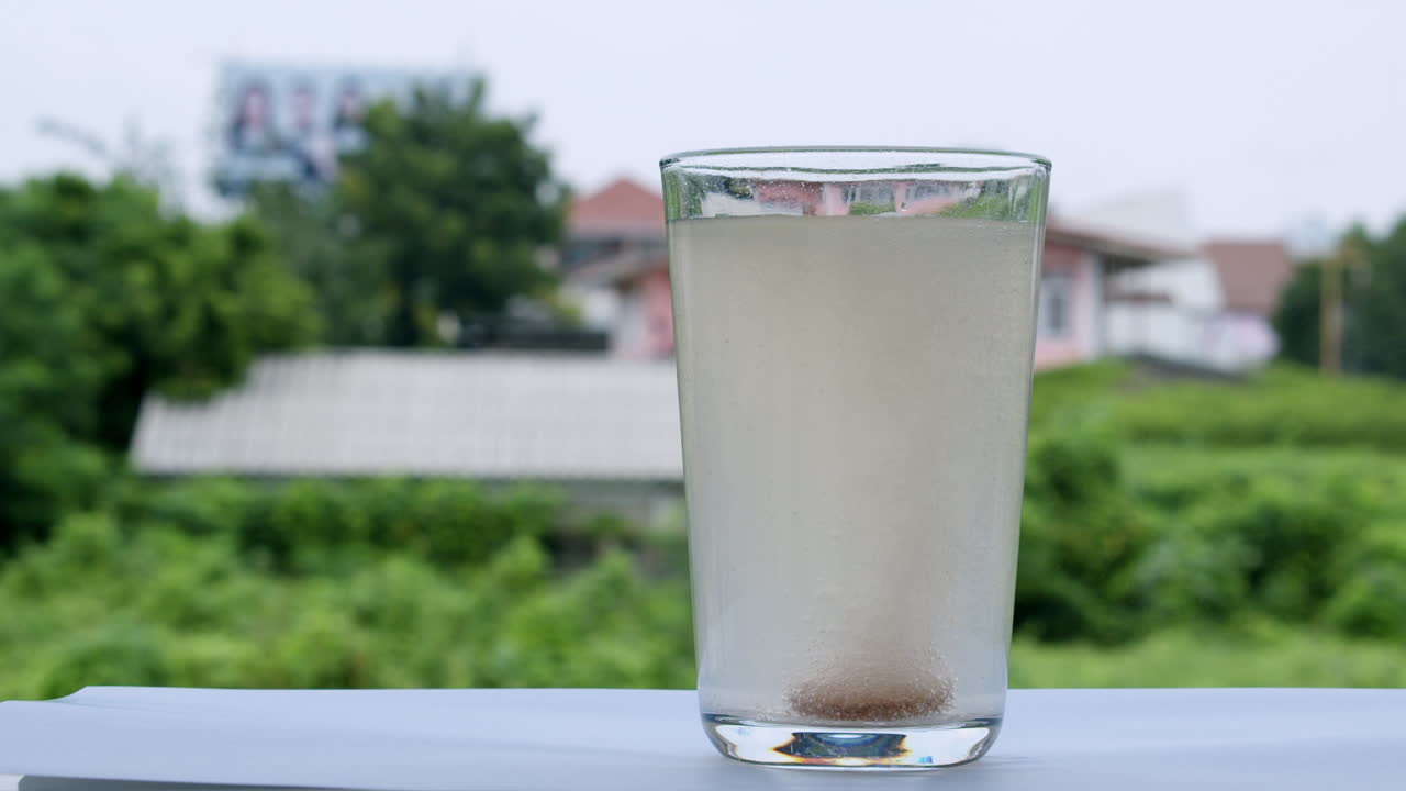 un vaso lleno de agua en el alféizar de la ventana está burbujeando con una tableta de bicarbonato de sodio antiácido dentro de la parte inferior del vaso