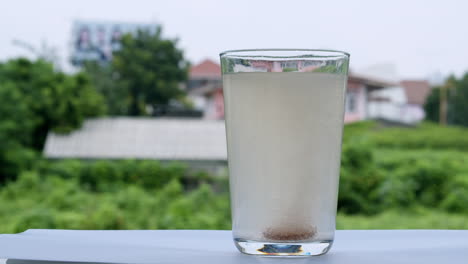 Un-Vaso-Lleno-De-Agua-En-El-Alféizar-De-La-Ventana-Burbujea-Con-Una-Tableta-De-Antiácido-De-Bicarbonato-De-Sodio-Dentro-Del-Fondo-Del-Vaso