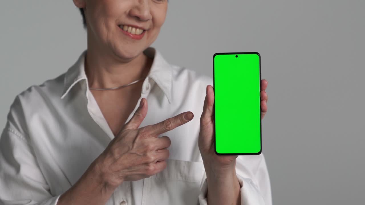 mujer asiática de mediana edad mostrando un teléfono inteligente con pantalla verde
