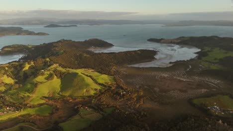 a stunning 4k 60fps aerial view of waiheke island at sunset. the drone glides over lush, rolling green hills and the pastoral coastline, bathed in beautiful golden hour light. a serene nz landscape