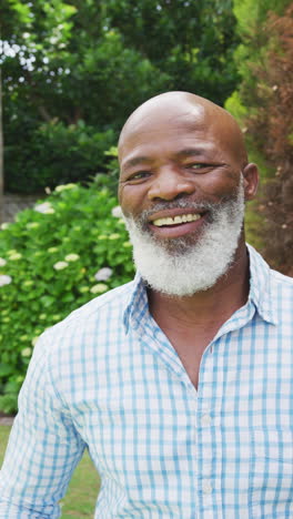 retrato de video vertical de un hombre mayor afroamericano feliz con barba sonriendo en el jardín