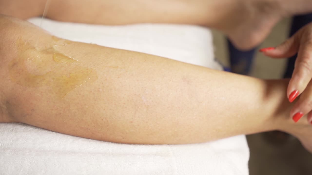 Primo piano di gambe femminili durante la depilazione con cera in un salone di bellezza. Rallentatore