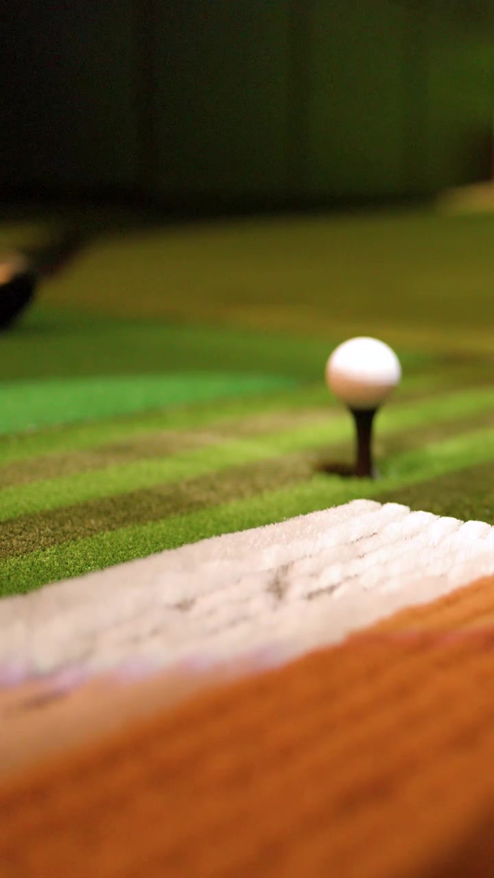 Primo piano di una mazza da golf che colpisce una palla su un tappeto simulatore indoor.