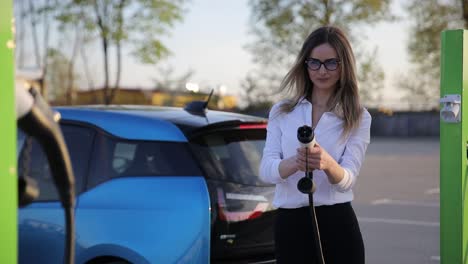 young woman with blonde hair charging electro car at the electric gas station. high quality 4k footage