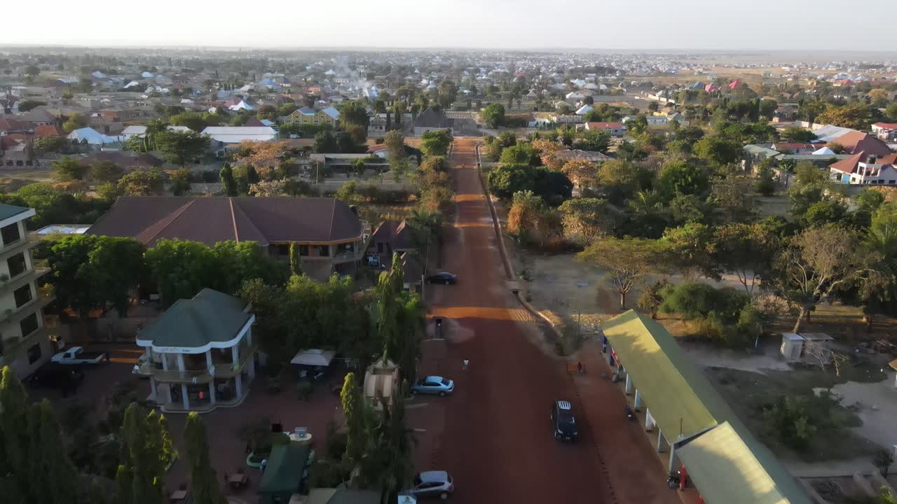 A 4K drone shot flying over a dirt road in Mwanza, Africa, near a hotel, tilting up to reveal the surrounding landscape.
