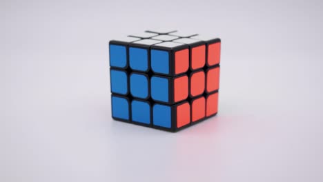 Primer-Plano-Del-Cubo-De-Rubik-Resuelto-Cayendo-En-El-Marco-Con-Un-Fondo-Blanco-Limpio