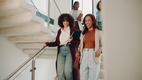 group of businesswomen laughing and talking while walking down the stairs in an office