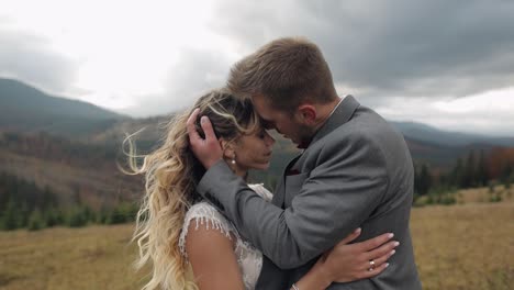 Lovely-young-newlyweds-bride-and-groom-embracing,-making-a-kiss-on-mountain-slope,-wedding-couple