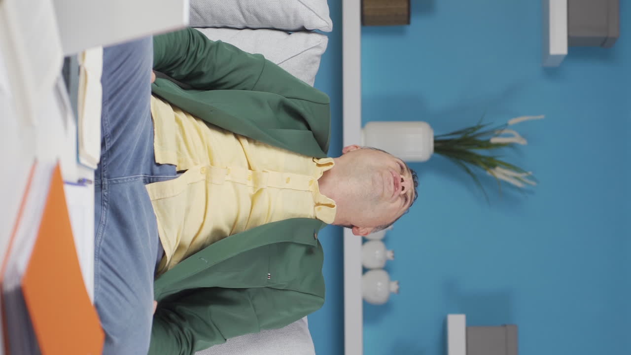 Vertikalvideo av en eldre hjemmekontorarbeider som fullfører arbeidet sitt og slapper av.