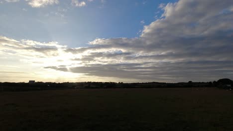 Time-lapse-sunset-clouds-changing-above-Welsh-agricultural-field-with-grazing-sheep-and-passing-traffic