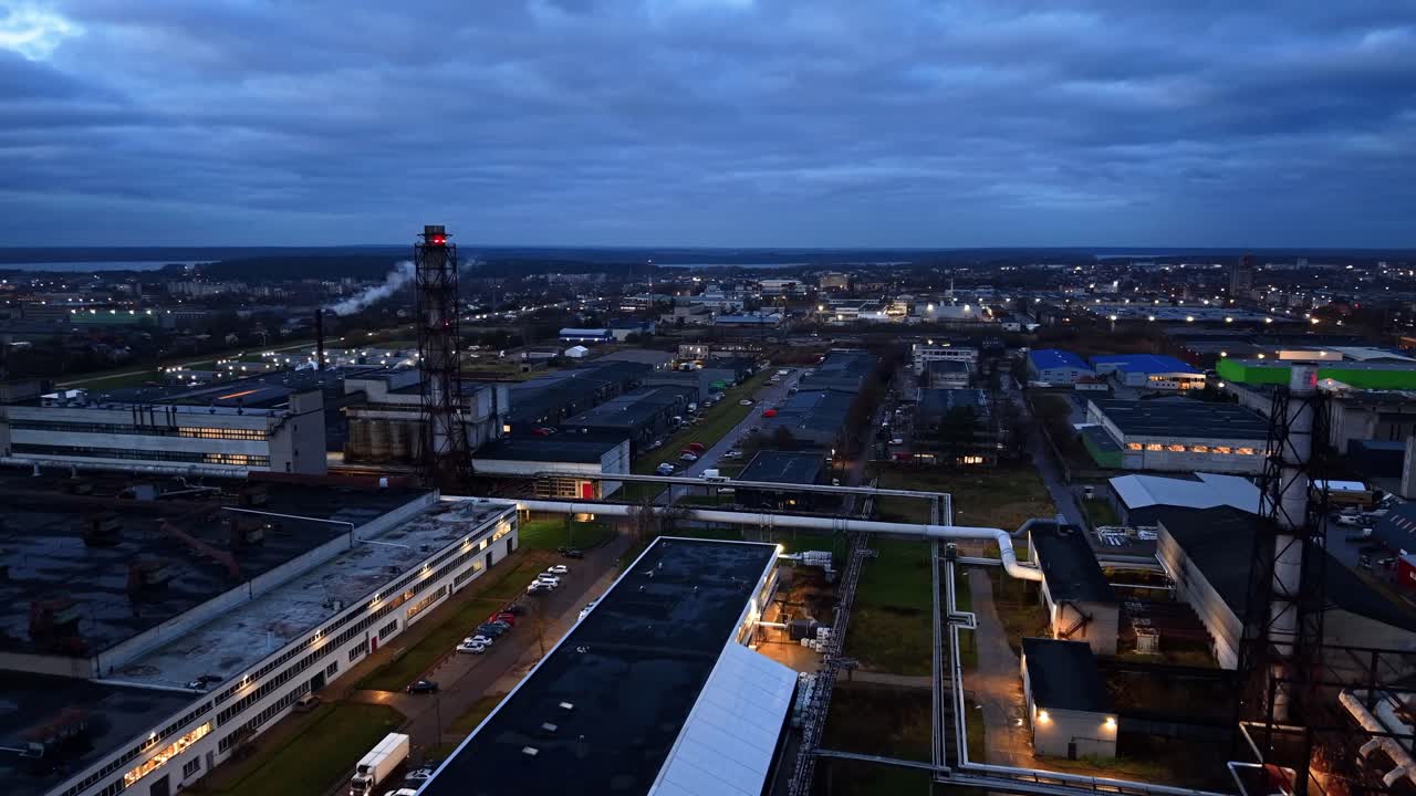 Drone video capturing an expansive industrial area at dawn. The setting sun casts a soft glow, highlighting factories and warehouses in a serene early morning atmosphere