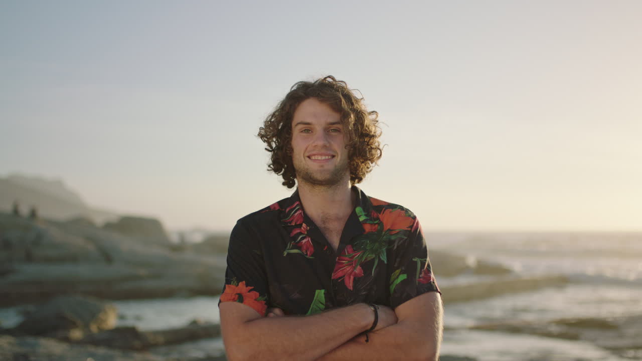 retrato de un joven relajado con los brazos cruzados sonriendo en la playa vistiendo una camisa hawaiana