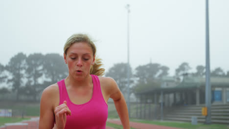 Front-view-of-Caucasian-female-athlete-exercising-on-running-track-at-sports-venue-4k