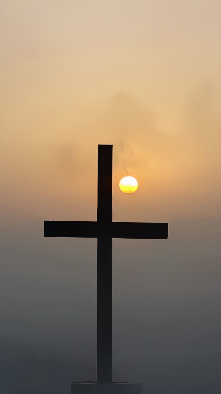 Vertical video: Sun rising behind wooden cross on misty hilltop at dawn, casting golden glow on fog