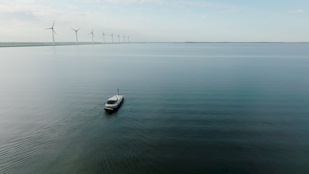Aerial shot of the Dutch boat Luxe Motor crossing the calm sea with a row of wind turbines in the background. in Holland