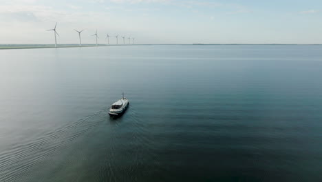 aerial shot of the dutch boat luxe motor crossing the calm sea with a row of wind turbines in the background. in holland