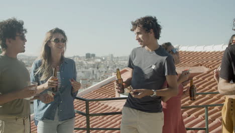 carefree friends talking together while eating pizza and drinking beer during a rooftop party