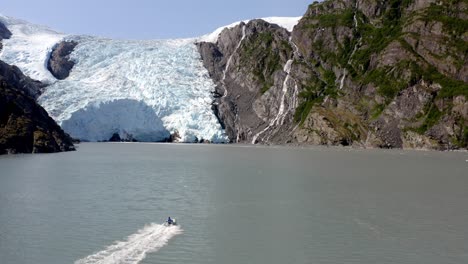 Aerial-View,-Massive-Glacier-Above-Cliffs-and-Speedboat-in-Glacial-Water,-Alaska-USA