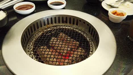 식탁에 조미료와 소스로 가득 찬 접시가 있는 환기가 잘 되는 탁상용 숯불 바베큐 그릴을 특징으로 하는 한국 바베큐 아시아 요리의 클로즈업