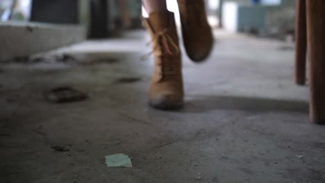 A-close-up-shot-of-a-pair-of-suede-leather-boots-walking-towards-the-camera-over-a-dirty-and-dusty-floor-inside-an-abandoned-building