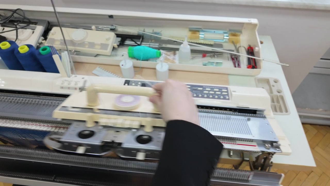 Top down view of a knitting workstation, including multiple spools of yarn, thread guides, and machine controls