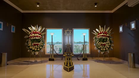 moving shot of the interior of a luxurious chapel of rest with two flower crowns, windows through which daylight enters and a star of david in the background