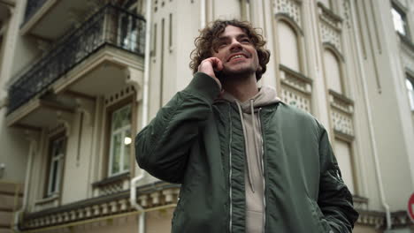 Smiling-man-speaking-mobile-phone-outdoor.-Hipster-using-cellphone-on-street.