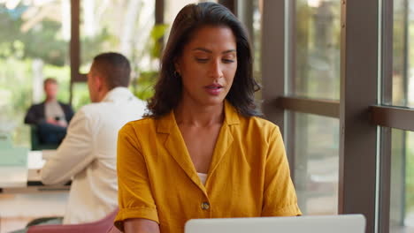 Mature-Businesswoman-Working-At-Desk-In-Open-Plan-Office-Looking-At-Watch