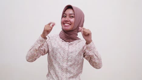 happy young asian muslim girl pointing presenting above and showing thumbs up to the camera