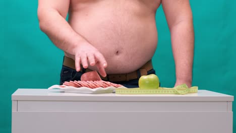 man with a fat belly chooses between sausage and a green apple. the concept of diet and willpower