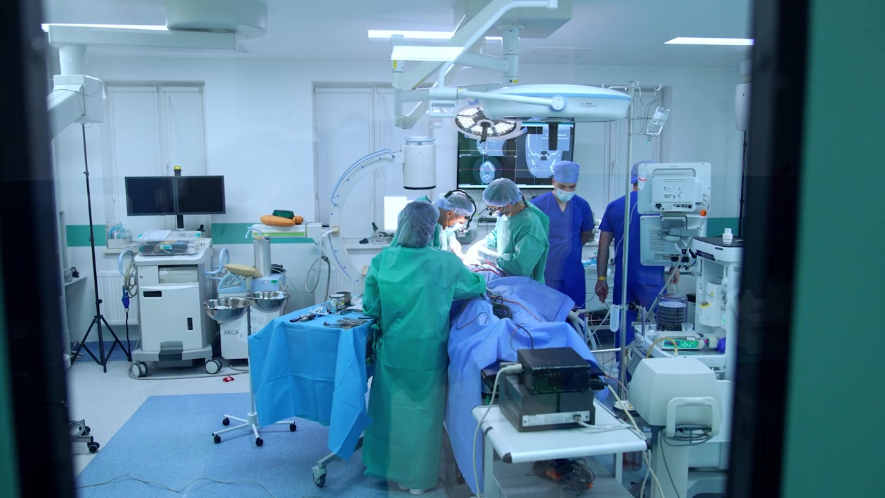 Medical team works in the modern surgery room. View through the window in the door to an operational theatre.