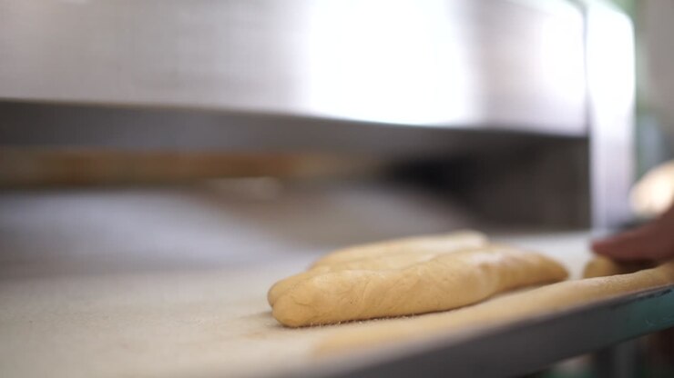 Close-up making bread in a bakery as a baker rolls out strands of dough after they come out of the bread roller