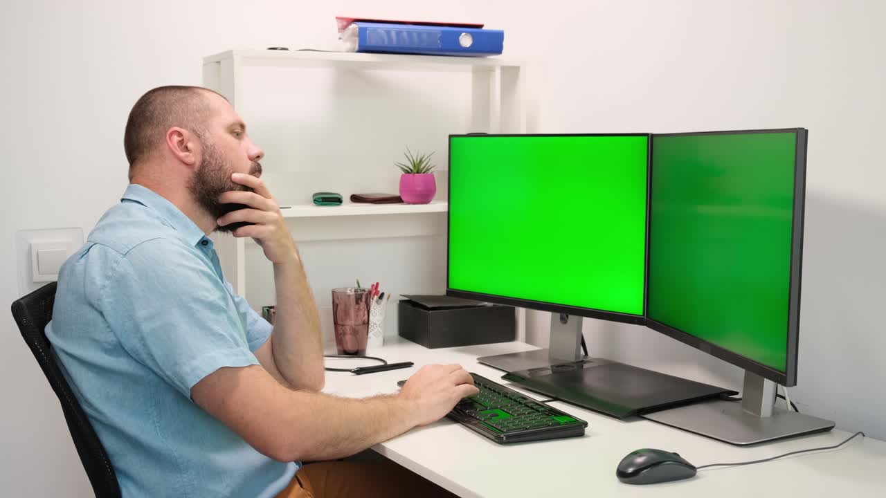 manos de un hombre barbudo escribiendo en el teclado en dos monitores con la pantalla verde