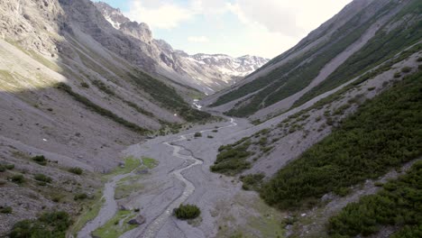 imágenes aéreas de drones que descienden lentamente hacia un espectacular valle glacial rodeado de montañas empinadas y pinos con parches de nieve y un río alpino en suiza
