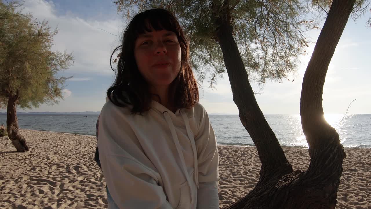 미소 귀여운 여자는 황금 시간, 중간 샷 해변에 나무 줄기에 앉아