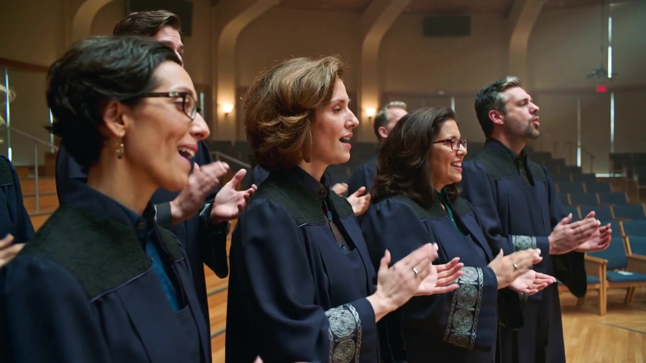 Hearing leader cue choir members in dark robes singing and clapping in church hall, patterned cuffs
