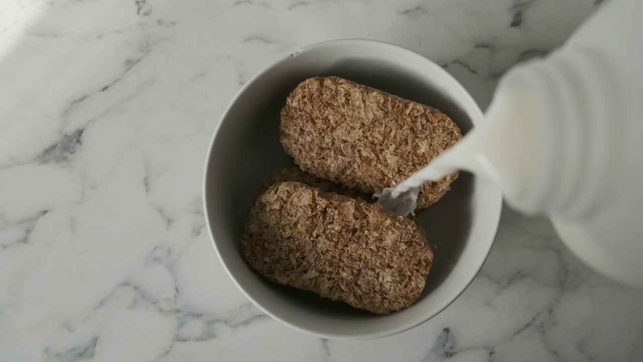 leche en cámara lenta vertida sobre mármol blanco de cereal de galleta weetabix