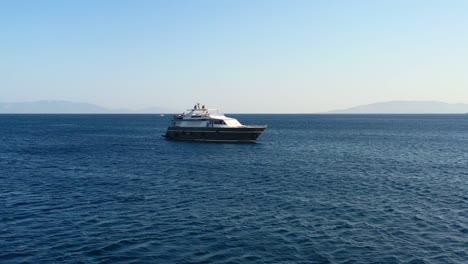 Drone-Aéreo-Que-Rodea-Un-Yate-Blanco-Y-Negro-Anclado-En-El-Agua-Azul-Del-Mar-Egeo-Entre-Turquía-Y-Grecia-En-Un-Día-Soleado-De-Verano