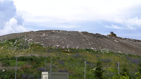 wide shot of mountain of rubbish as landfill hill with a bulldozer on top of it