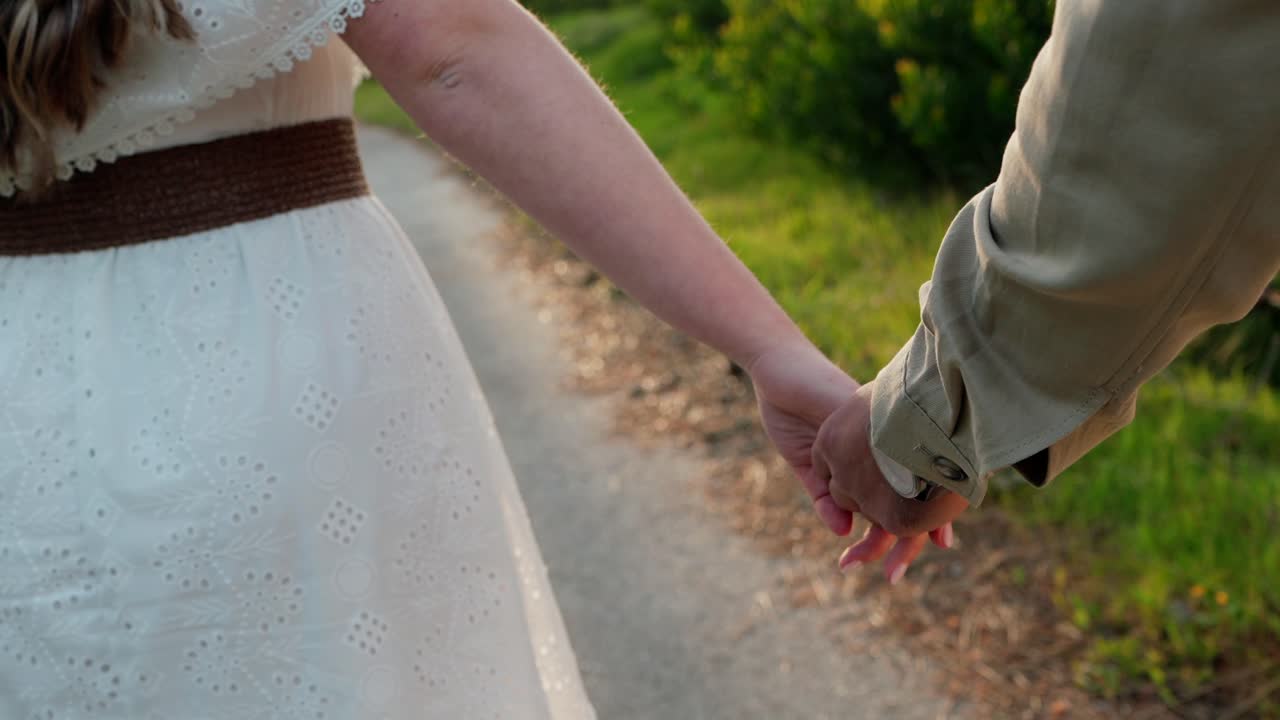 close up of couple holding hands walking on rural path in warm sunlight