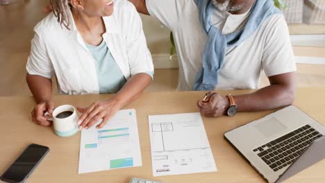 High-angle-view-of-african-american-senior-couple-doing-paperwork-using-laptop-at-home,-slow-motion