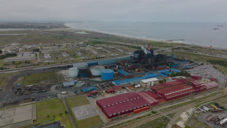 Aerial-footage-of-industrial-site-on-seaside.-Factory-with-striped-chimneys-and-production-halls-near-coastal-highway.-Port-Elisabeth,-South-Africa